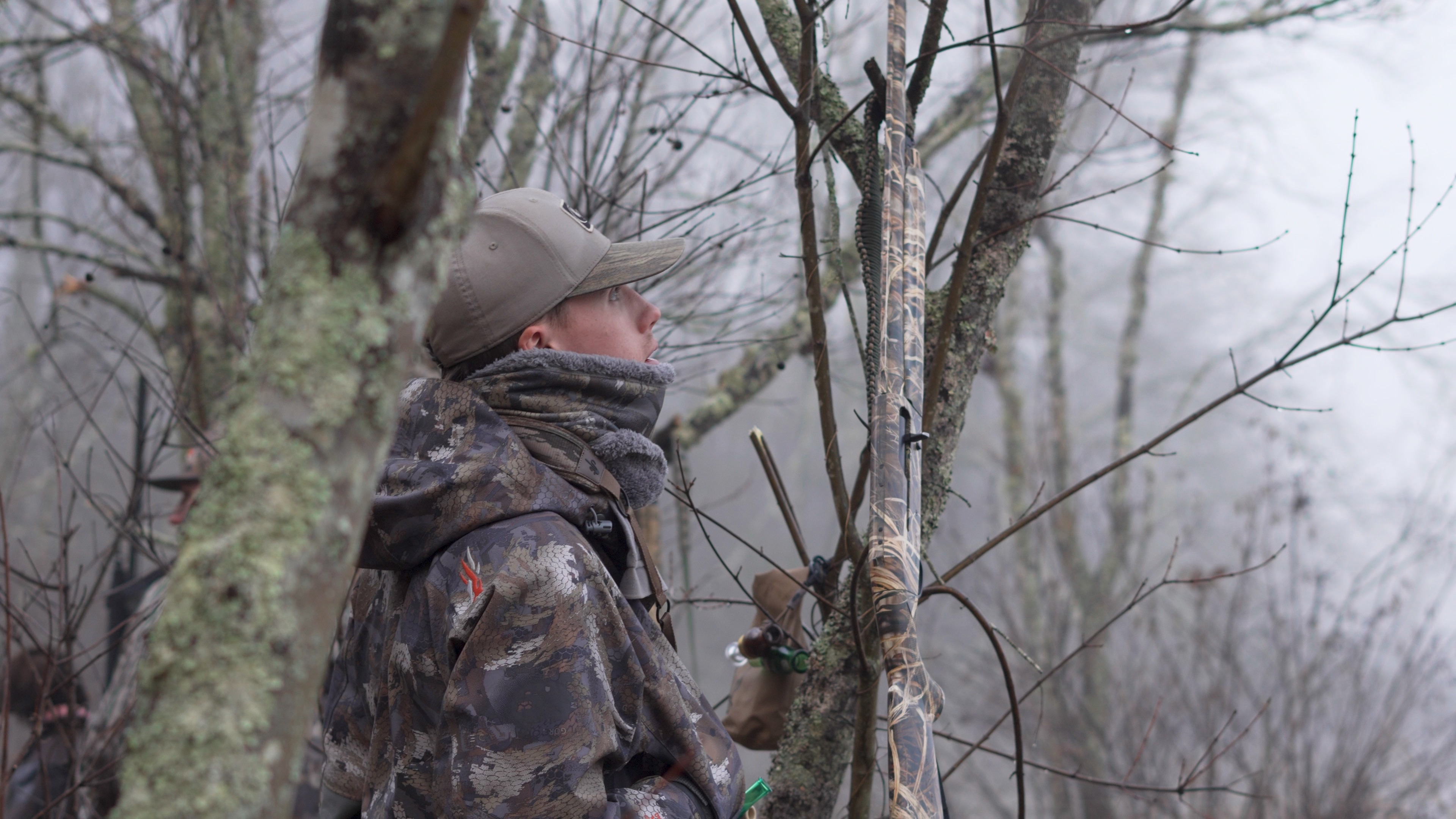 Hunter standing among trees with outdoor gear