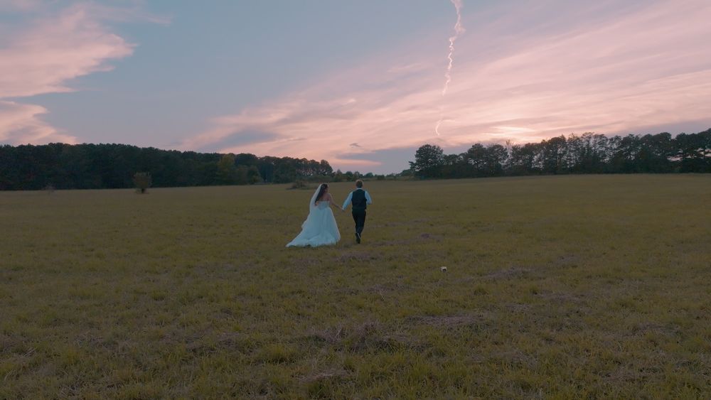 Melyiah and Austin walking hand in hand across an open field at sunset in Temple, Georgia