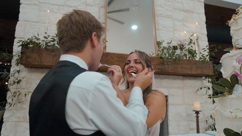 Melyiah and Austin feeding each other wedding cake beside a stone fireplace at The Grove at Defoor Farms